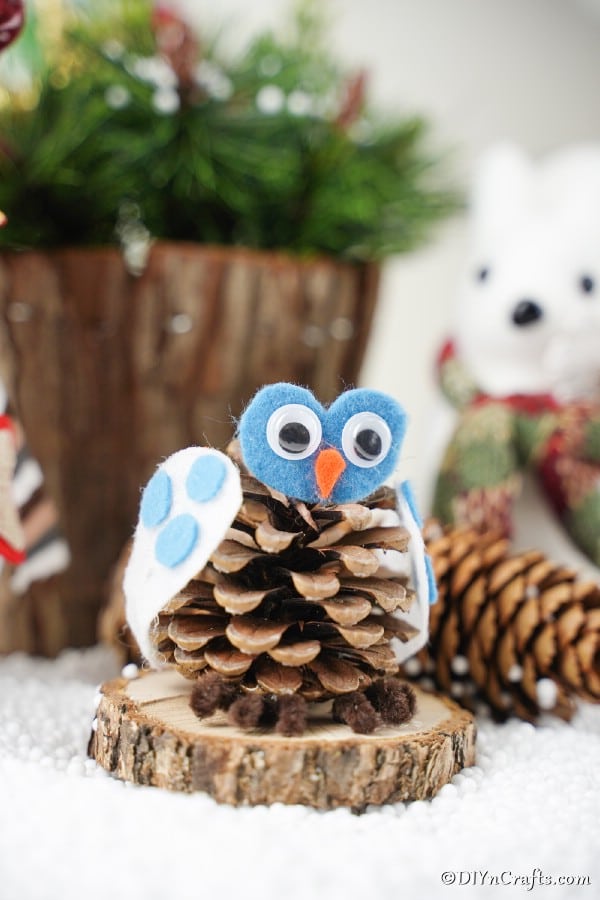 A pinecone owl decoration sitting on a wood slice