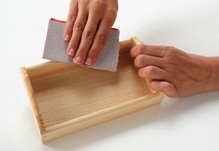 Sanding a small wood tray with a piece of sandpaper