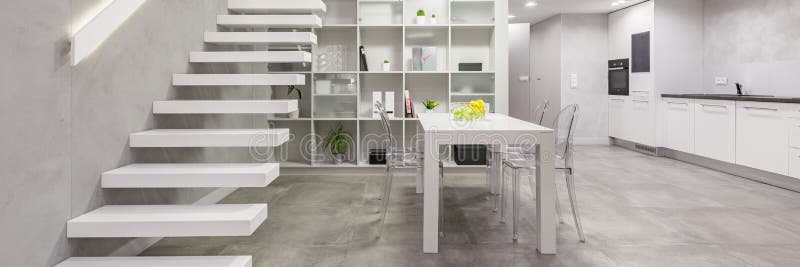 Apartment with modern white staircase. Loft apartment with modern white mezzanine staircase, dining table with chairs and open kitchen stock image