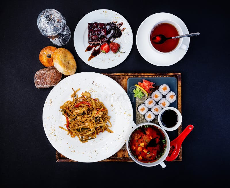 Asian food set. Fried noodles with chicken, miso soup, sushi with salmon, cup of tea and cake. Top view. Asian style food concept composition stock photos