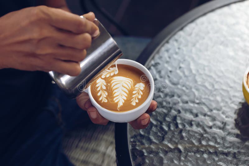 Barista pouring milk foam for making coffee latte art with pattern the leaves in a cup stock photos