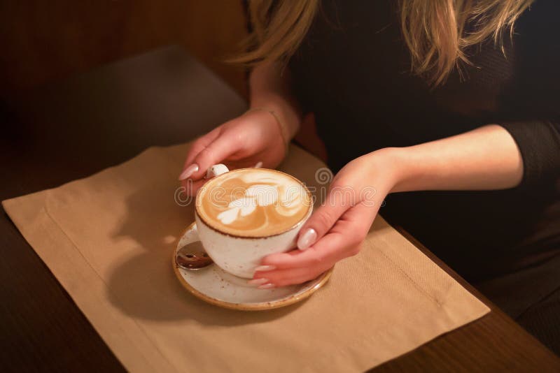 Close-up in the cafe hands of a girl holding a Cup of coffee with a pattern in coffee shops,in the cafe. Close-up in the cafe hands of a girl holding a Cup of royalty free stock photos