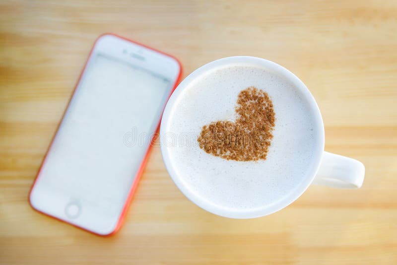 Coffee with a heart pattern and a phone. A cup of coffee with a pattern of cinnamon in the form of a heart and in the background a phone with a white screen royalty free stock photography