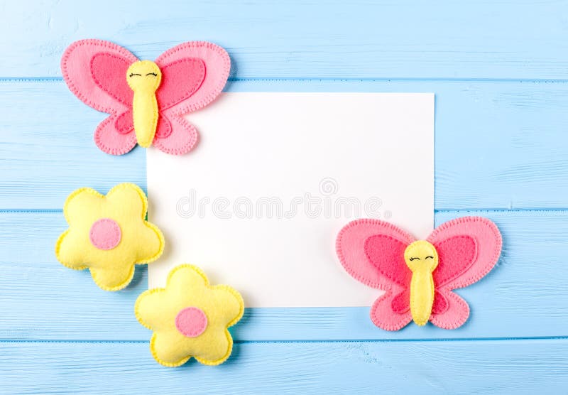 Craft pink and yellow butterfly and flowers with white paper, copyspace on blue wooden background. Hand made felt toys. Abstract s stock photo
