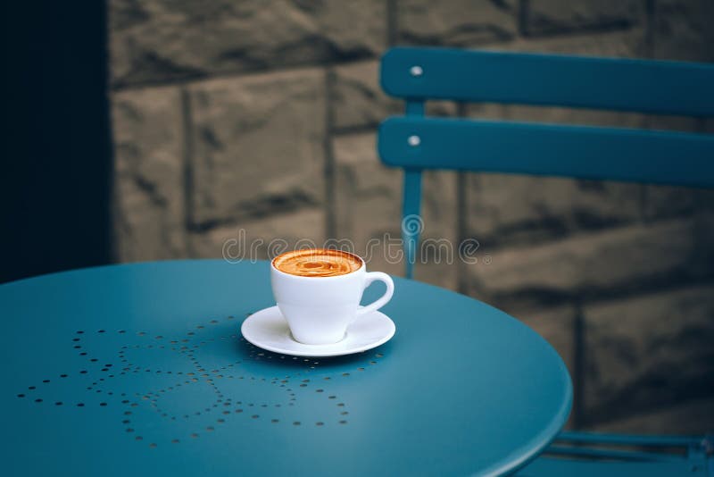 Cup of coffee in street cafe. White cup of coffee with crema on a round blue table with a pattern in street cafe stock photography