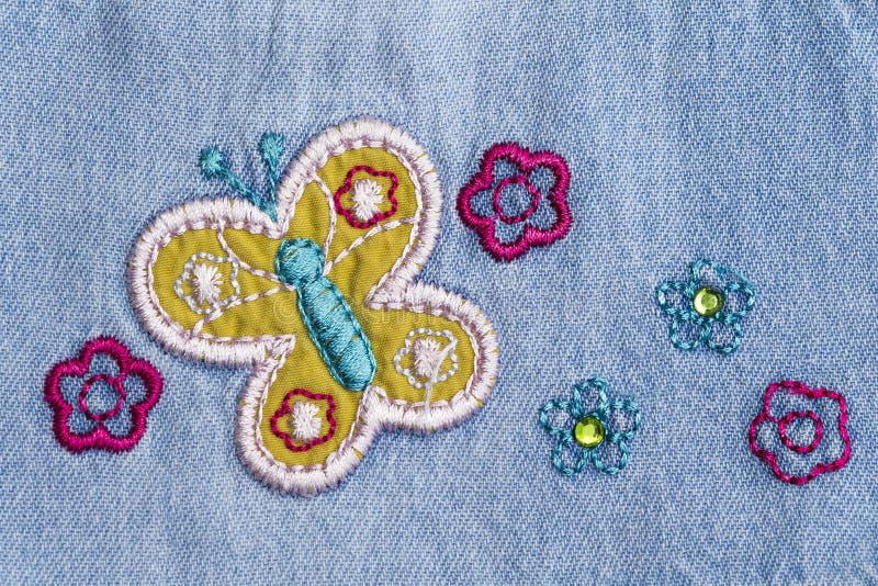 Denim with an embroidery. Fragment of the denim fabric with embroidery in the form of flowers and butterflies stock photos
