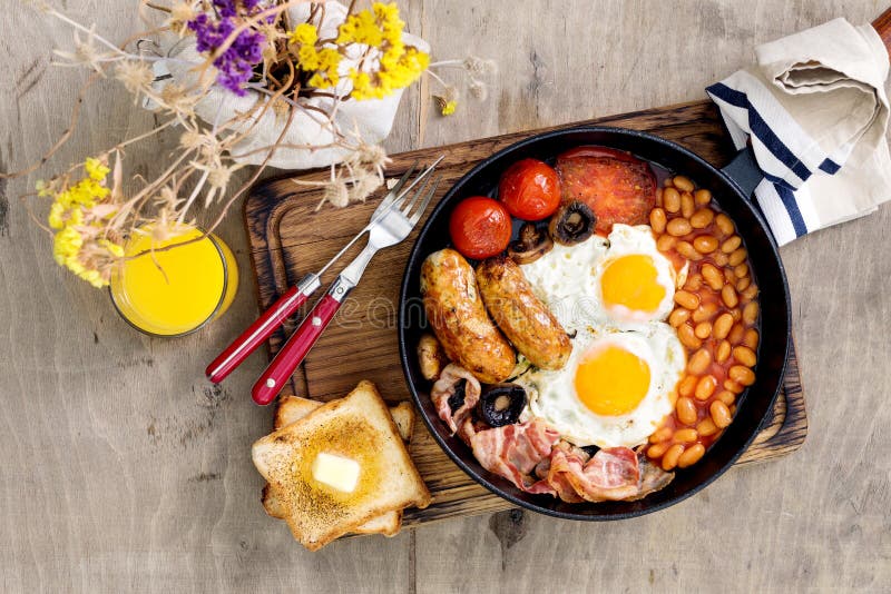 English breakfast in cast-iron frying pan with bouquet of wildfl royalty free stock image