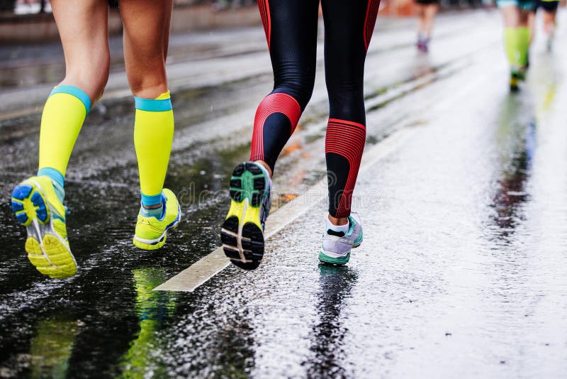 Feet two girls athletes running. On wet street urban marathon stock photos