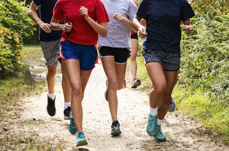 Front view of a group of runners training on a dirt path in the woods. A group of boys and girls cross country runners training together on a dirt path in a stock image