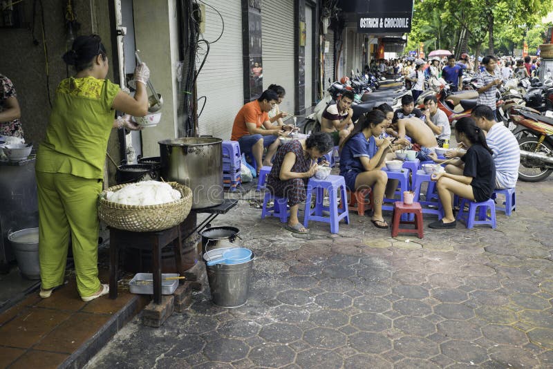 Hanoi, Vietnam - Sep 2, 2015: People eating Vietnamese traditional noodle soup Pho on sidewalk. Eating on pavement is common in Ha royalty free stock photography