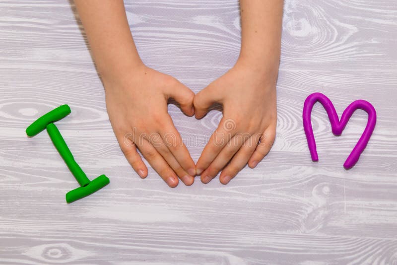 I love mom text from plasticine with kid hands on white wooden background. Happy mothers day. Fun kids handmade craft stock image