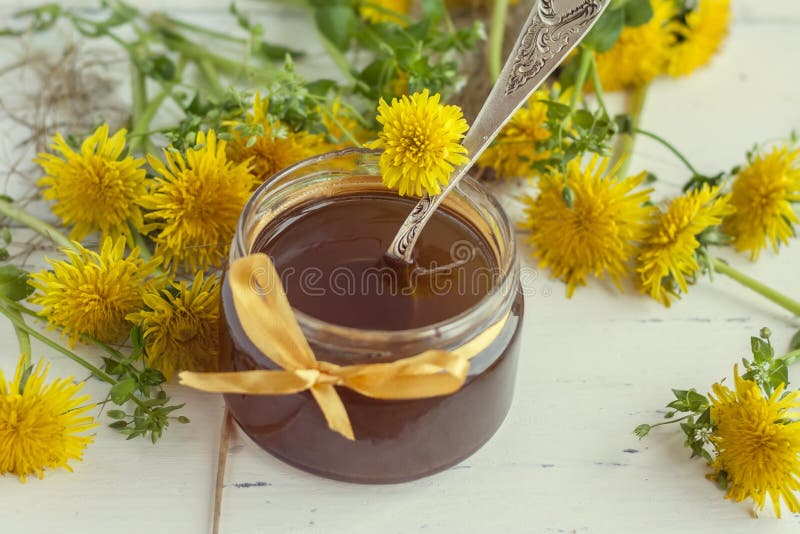 Jar of homemade delicious dandelion jam on a light wooden table with yellow dandelions. Flower dandelion syrup. Useful. Preservation for the winter royalty free stock photo