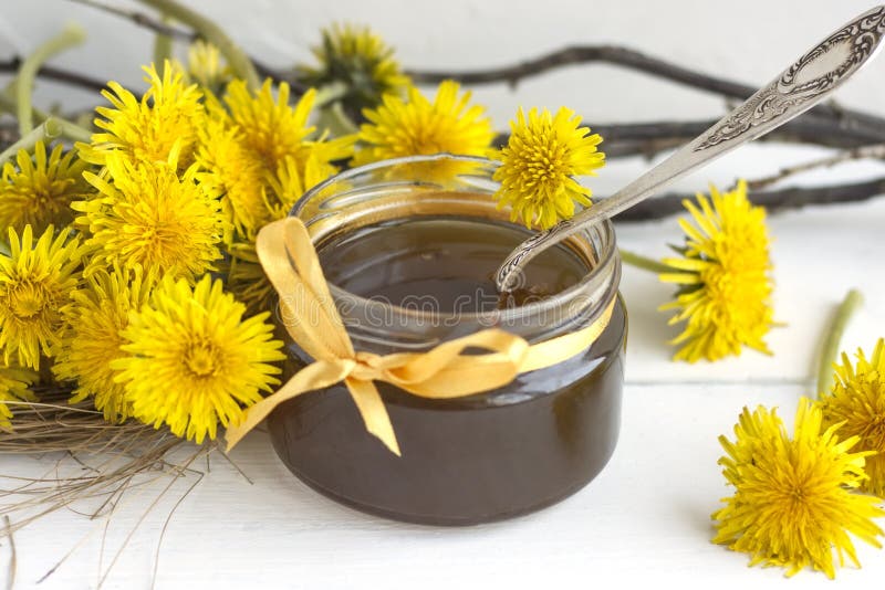 Jar of homemade delicious dandelion jam on a light wooden table with yellow dandelions. Flower dandelion syrup. Useful. Preservation for the winter royalty free stock image