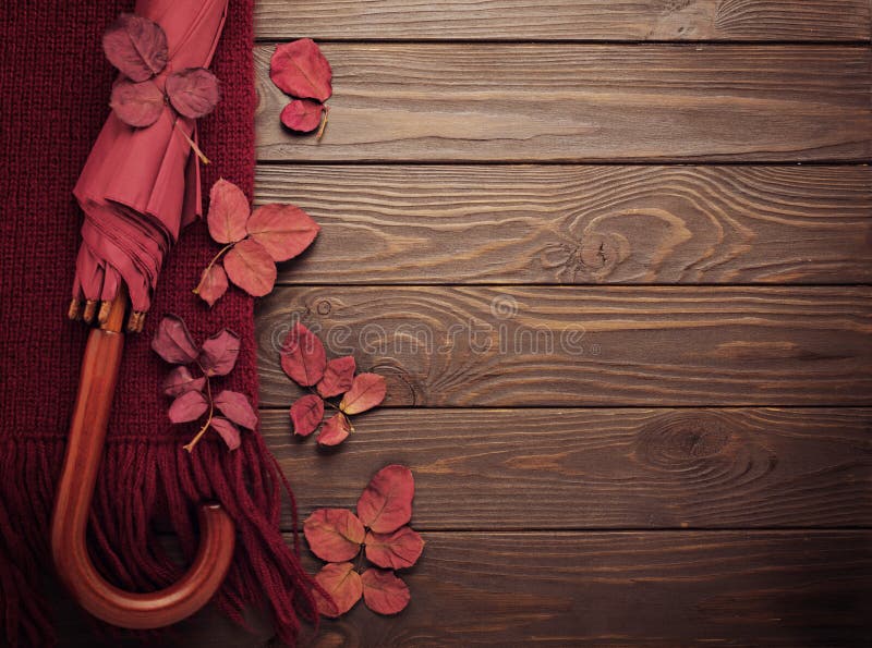 Knitted scarf of burgundy color with autumn leaves and an umbrella on a dark wooden background. stock photos