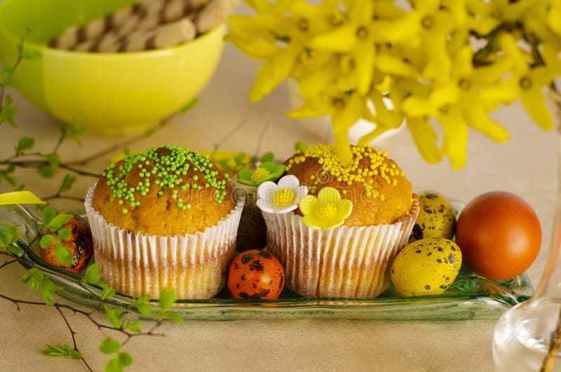 Muffins decorated with sprinkles, flowers of mastic, colored easter quail eggs on a kitchen table. stock image