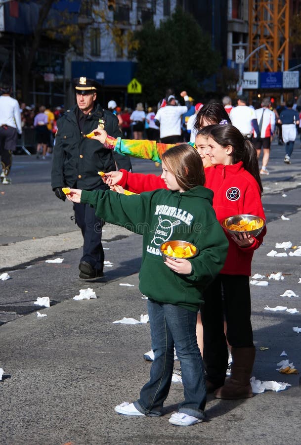 Young Girls Handing Snacks to Marathon Runners. New York City, NY USA. Nov 2008. Young girls handing out oranges to runners by a patrolling police officer during royalty free stock photo