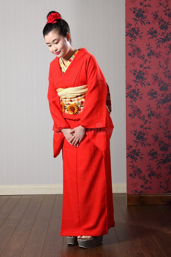 Oriental model in red Japanese kimono bowing. Respectful bow by beautiful young oriental model in red Japanese kimono robe garmant complete with obi sash and royalty free stock photography