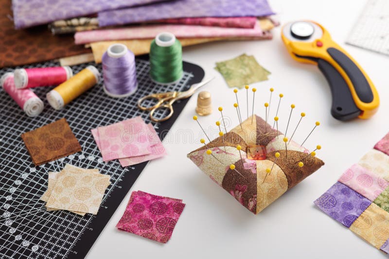 Pin cushion, stacks of square pieces of fabric, pile of patchwork fabrics, quilting and sewing accessories royalty free stock image