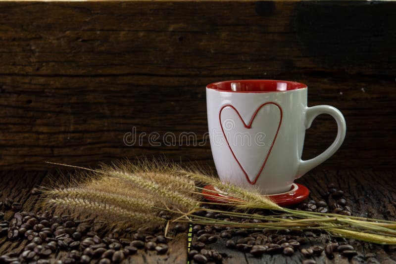 Red and white coffee cup with heart shape pattern, dry grass flowers and coffee beans on wood table. And wooden wall stock image