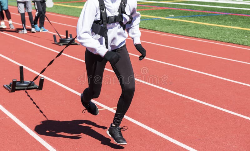 Runners pulling weighted sleds on a track. Runners, sprinters on a boys and girls high school track and field team run while pulling a sled with weights on it royalty free stock images