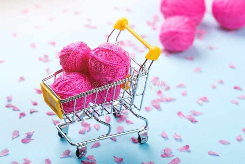 Shopping cart full of wool knitting balls. Knitting background. Pink wool yarns. Colorful pink threads on blue paper background. stock image
