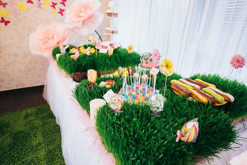 A table with a festive cake with mastic flowers and cookies. Kandy bar is decorated with grass on which cake and lollipops.  royalty free stock photos