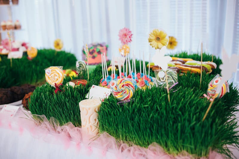 A table with a festive cake with mastic flowers and cookies. Kandy bar is decorated with grass on which cake and lollipops.  stock photos