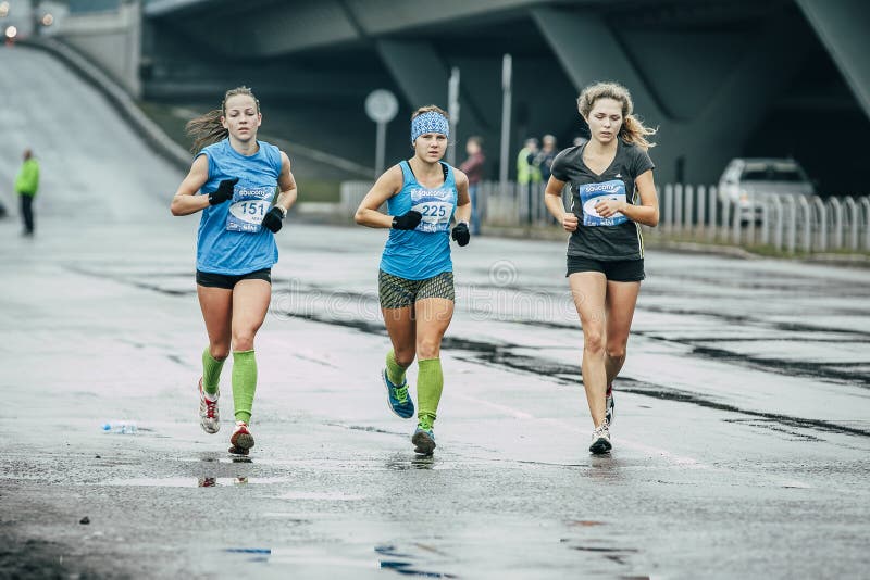 Three girls runners run on wet asphalt. Omsk, Russia - September 20, 2015: three girls runners run on wet asphalt during Siberian international marathon stock image