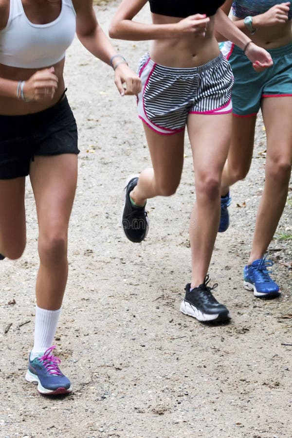 Three high school girls running on a dirt trail in the summer. Three high school girls cross country runners training together in the summer on a dirt path side royalty free stock image