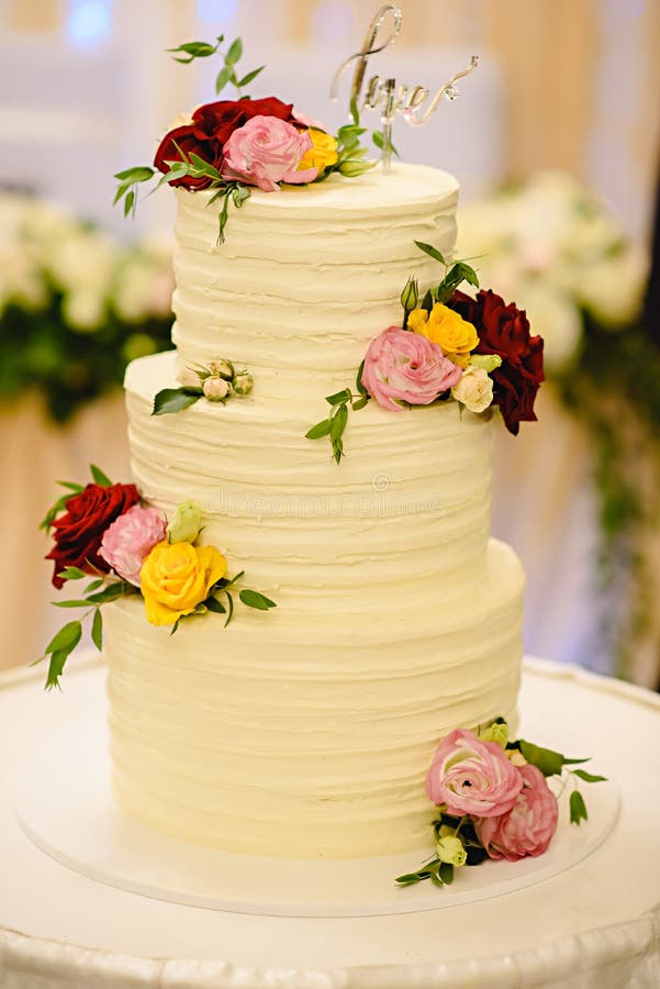 Three-tiered white wedding cake decorated with flowers from mastic on a white wooden table. stock images