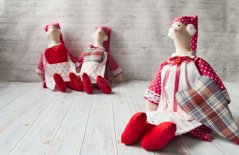 Three tilde dolls in red dresses, and white aprons, and red kalpaks sit on a light background. Interior dolls. There is stock photo