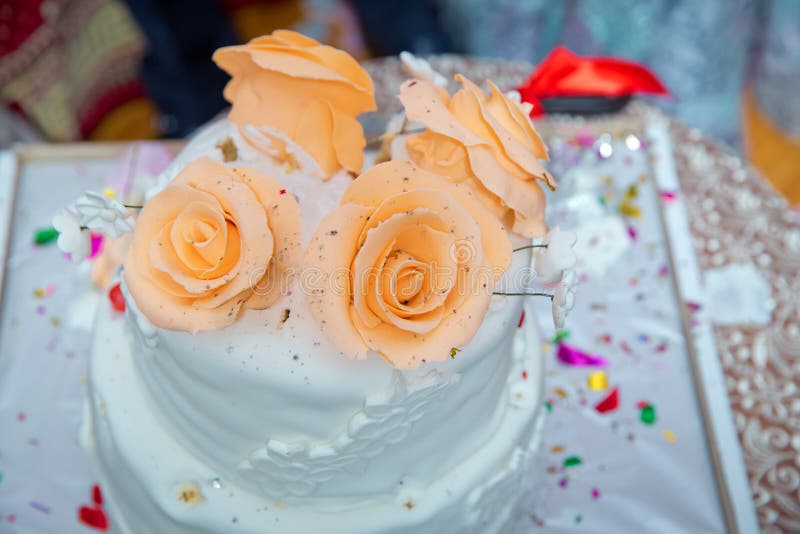 White cake yellow four flowers . Beige 4 tiered wedding cake decorated with mastic roses stands on the table on fabric background stock images