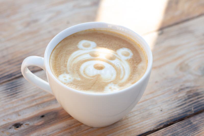 White сup of coffee on a wooden table with a bear pattern. White сup of coffee on a wooden table. Cappuccino with a bear pattern and sunlight in mug royalty free stock photo