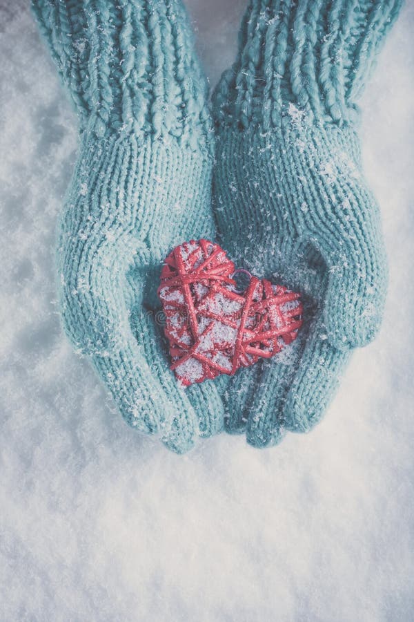 Woman hands in light teal knitted mittens are holding beautiful glossy red heart on snow background. Love, St. Valentine concept stock images