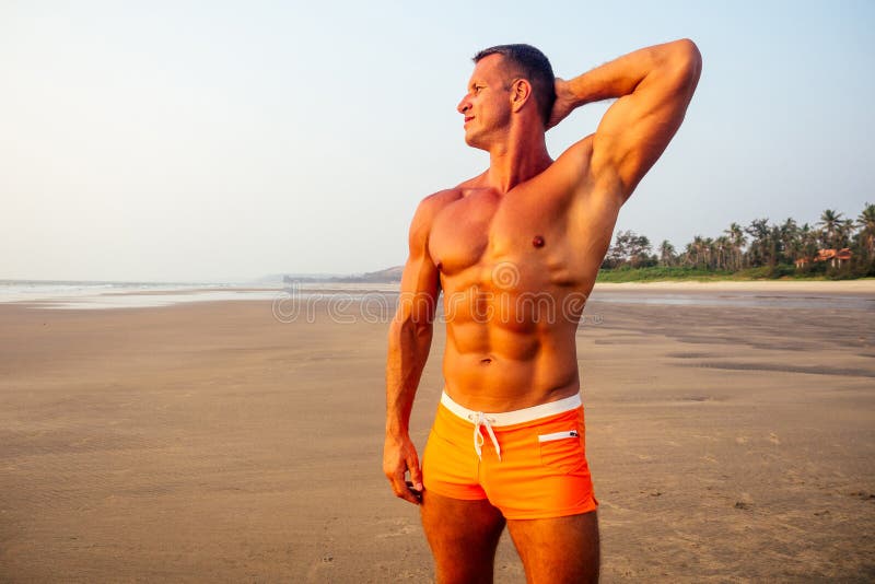 Young handsome man applying cream sunscreen lotion on the sea beach.Sexy male model athlete bodybuilder posing the royalty free stock image